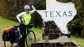 A cyclist leans against a welcome to Texas sign