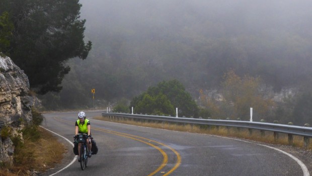 A bicyclist rides through the fog on a curvy road.