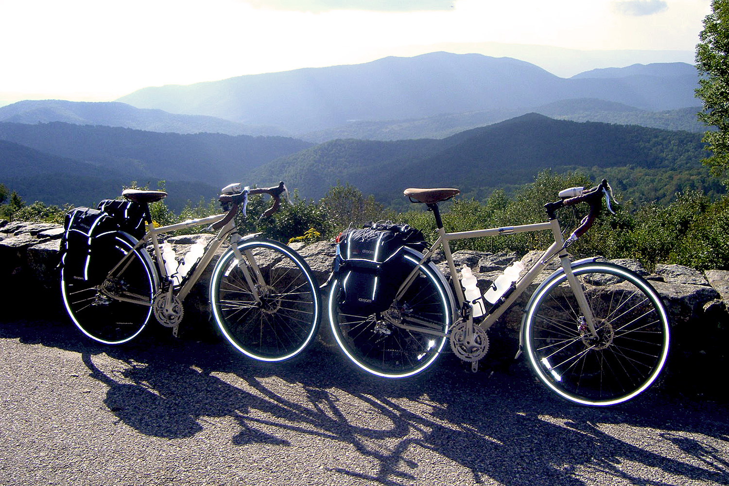 Two loaded touring bicycles leaning against a wall with mountains in the background