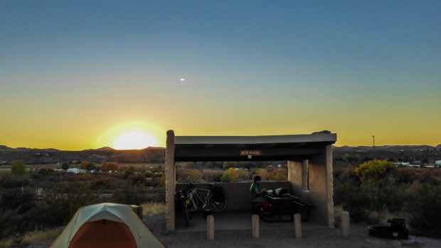 The sun sets behind a tent and picnic structure.
