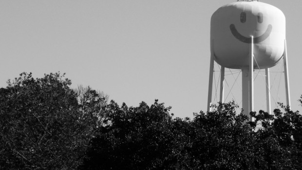 A water tower with a painted smiley face rises above the trees.