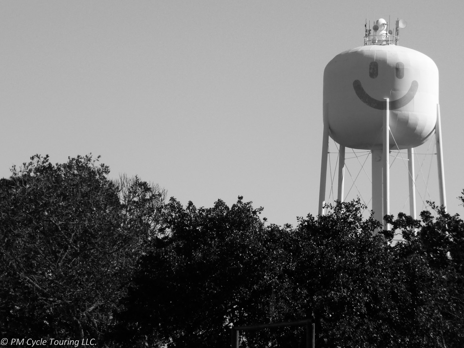 A water tower with a painted smiley face rises above the trees.