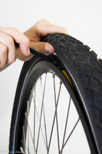 Prying the tire over the rim by inserting a tire lever.