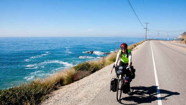 A bicycle rider on a fully loaded touring bicycle rides on the shoulder near the ocean