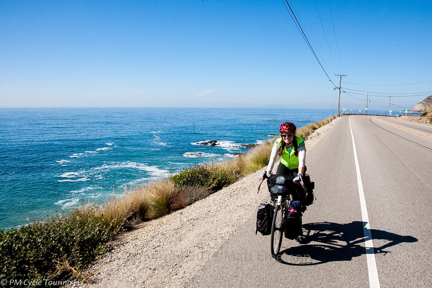 A bicycle rider on a fully loaded touring bicycle rides on the shoulder near the ocean