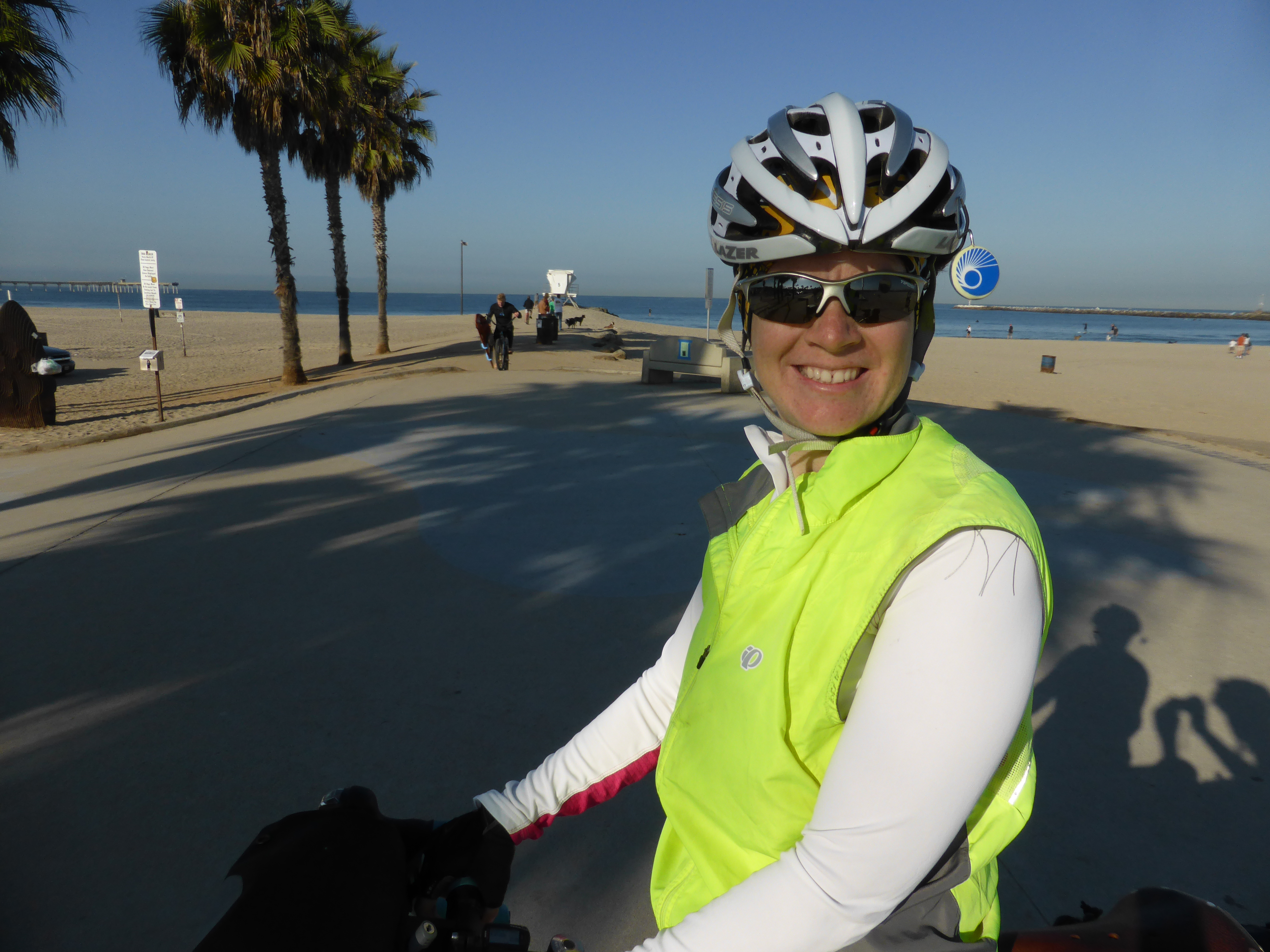 A cyclist faces the camera and smiles with a bike path in the background.