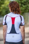 A woman wearing a short sleeved, white cycling jersey, the back side.