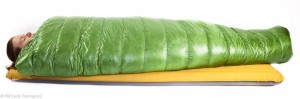 A woman laying inside a green sleeping bag on top of an air pad.