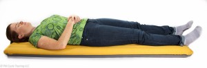 A woman lays on a yellow synmat sleeping pad