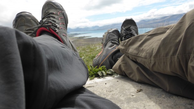 Lake Tekapo in the distance, two sets of legs and shoes in the foreground